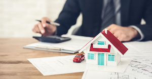 House model standing on property plans as man in a suit is calculating its price. SAM Conveyancing's guide to how does a surveyor value a property? House model standing on property plans as man in a suit is calculating its price. SAM Conveyancing's guide to how does a surveyor value a property?