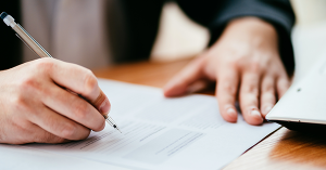 Man in a suit signing a form in an office. Landlord Statutory Declaration. A guide from SAM Conveyancing on how to file a statutory declaration form