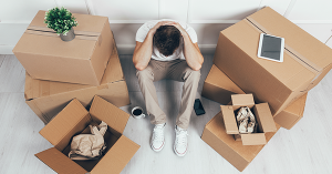 A man sits in a pile of boxes, overcome with moving house stress. SAM Conveyancing's top tips for managing the stress of moving house.