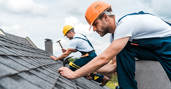What are leasehold service charges? Explained by SAM conveyancing. Two workers in hard hats and overalls nail tiles to a roof