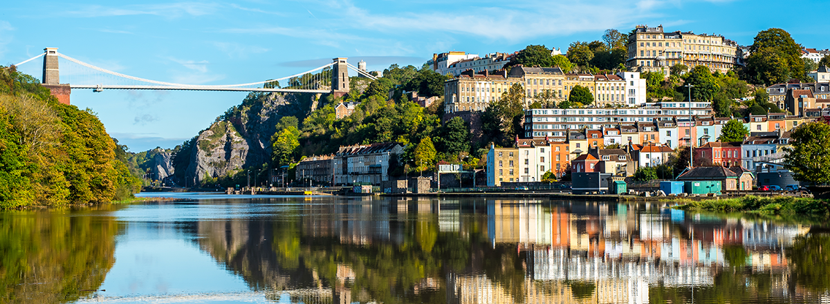 Wide pan photo of the Clifton suspension bridge (left) and Hotwells area of Bristol, on a calm, sunny day, taken from the river Avon, which reflects the landscape. SAM Conveyancing analyse the latest Land Registry data on the Bristol housing market