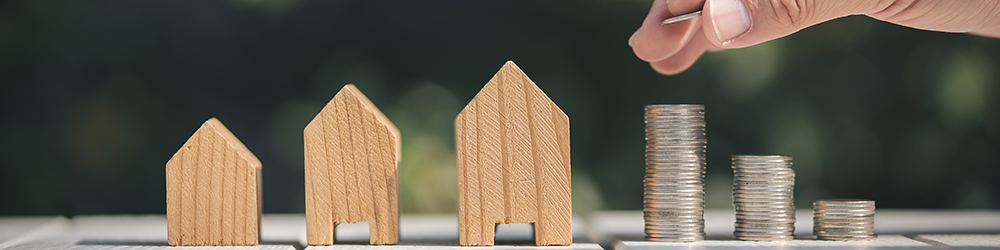 Weigh value and price when you compare conveyancing quotes. A hand adds a coin to one of 3 different sized stacks of coins next to a wooden block house.
